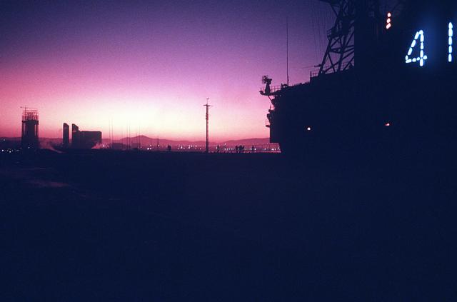 The island of the aircraft carrier USS MIDWAY (CV-41) is silhouetted against the early morning sky as the ship prepares to get u