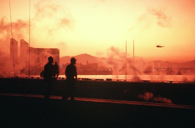 Flight deck crewmen aboard the aircraft carrier USS MIDWAY (CV-41) are silhouetted against the early morning sky as the ship pre