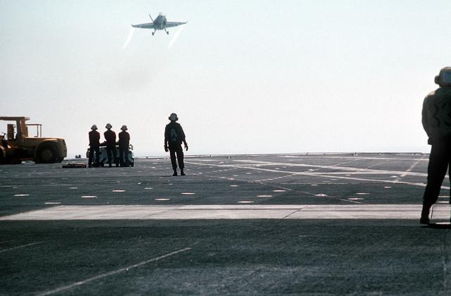 Arresting gear crewmen aboard the aircraft carrier USS MIDWAY (CV-41) watch as a Strike Fighter Squadron 151 (VFA-151) F/A-18A H