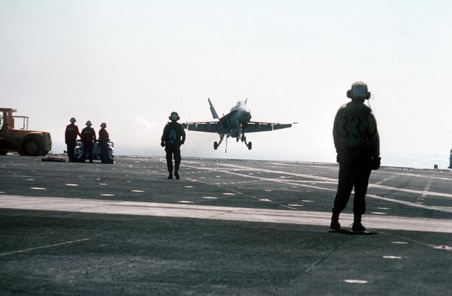 Arresting gear crewmen aboard the aircraft carrier USS MIDWAY (CV-41) watch as a Strike Fighter Squadron 151 (VFA-151) F/A-18A H