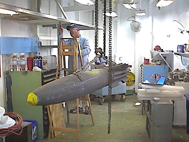 Bob Solomon (LCDR AO Ret.) painting the AME Shop (Space C-150) on the ship, with MK-82 Mod 1(inert) on hoist making ready for di