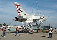 Crane riggers from the U.S. Navy Public Works Center (PWC) guide a F-8K Crusader aircraft onto a floating barge for delivery to
